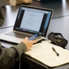 Student holding a phone and looking at a script open on a laptop computer.
